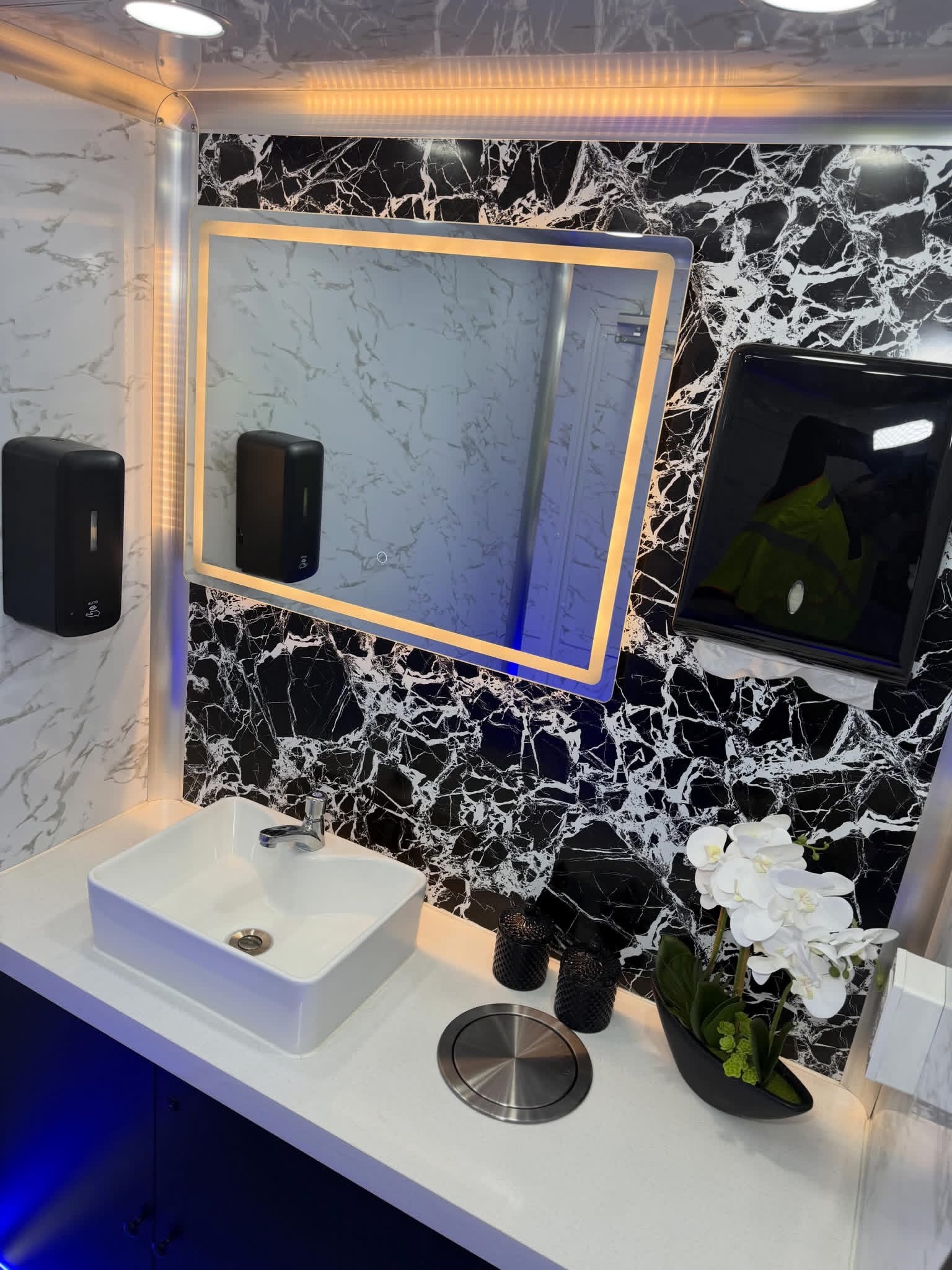 Close-up of marble walls, lit mirror and touch-free dispensers