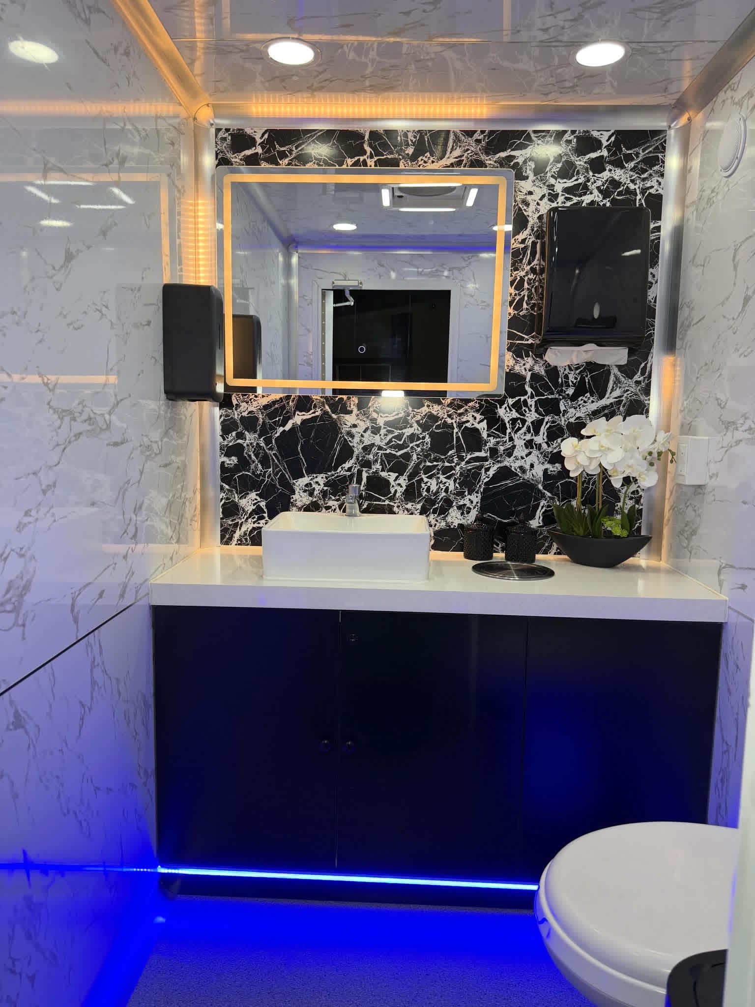 Luxury restroom trailer interior with marble walls, gold-lit vanity mirror and vessel sink