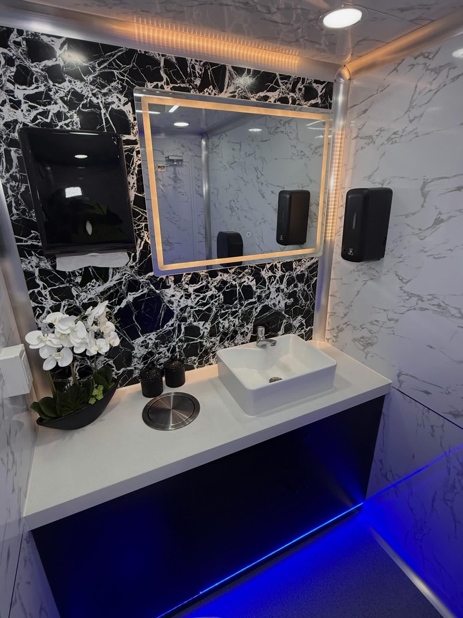 Marble vanity with gold LED mirror, vessel sink and orchid inside the 951 Luxury Restrooms trailer