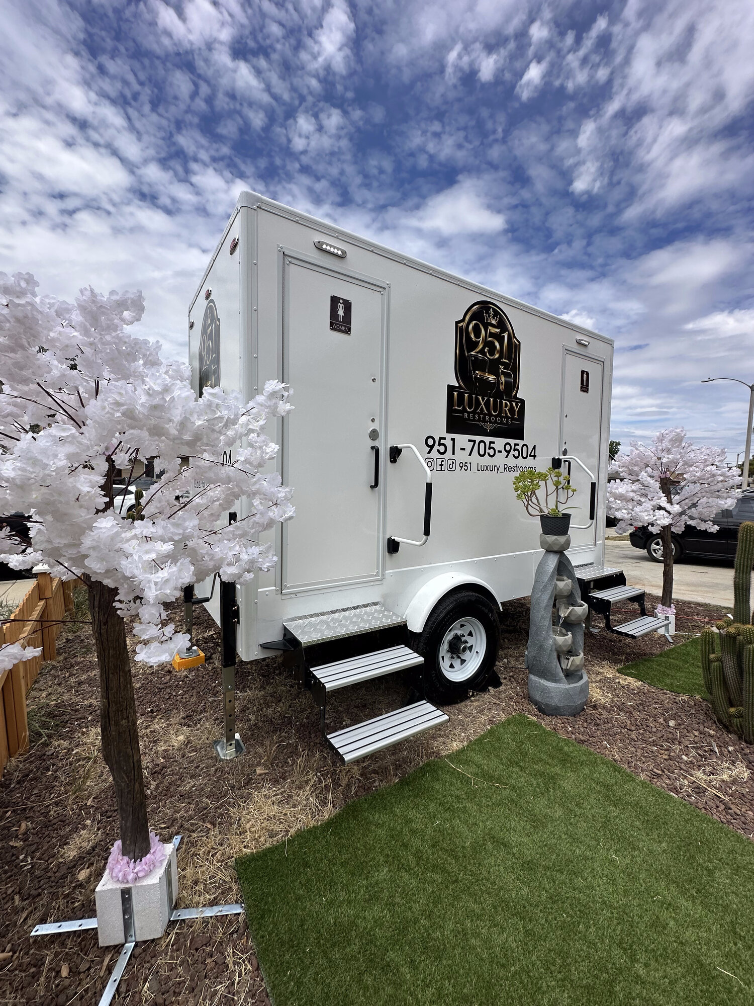 951 Luxury Restrooms trailer exterior styled with cherry blossom trees, turf and stone fountain